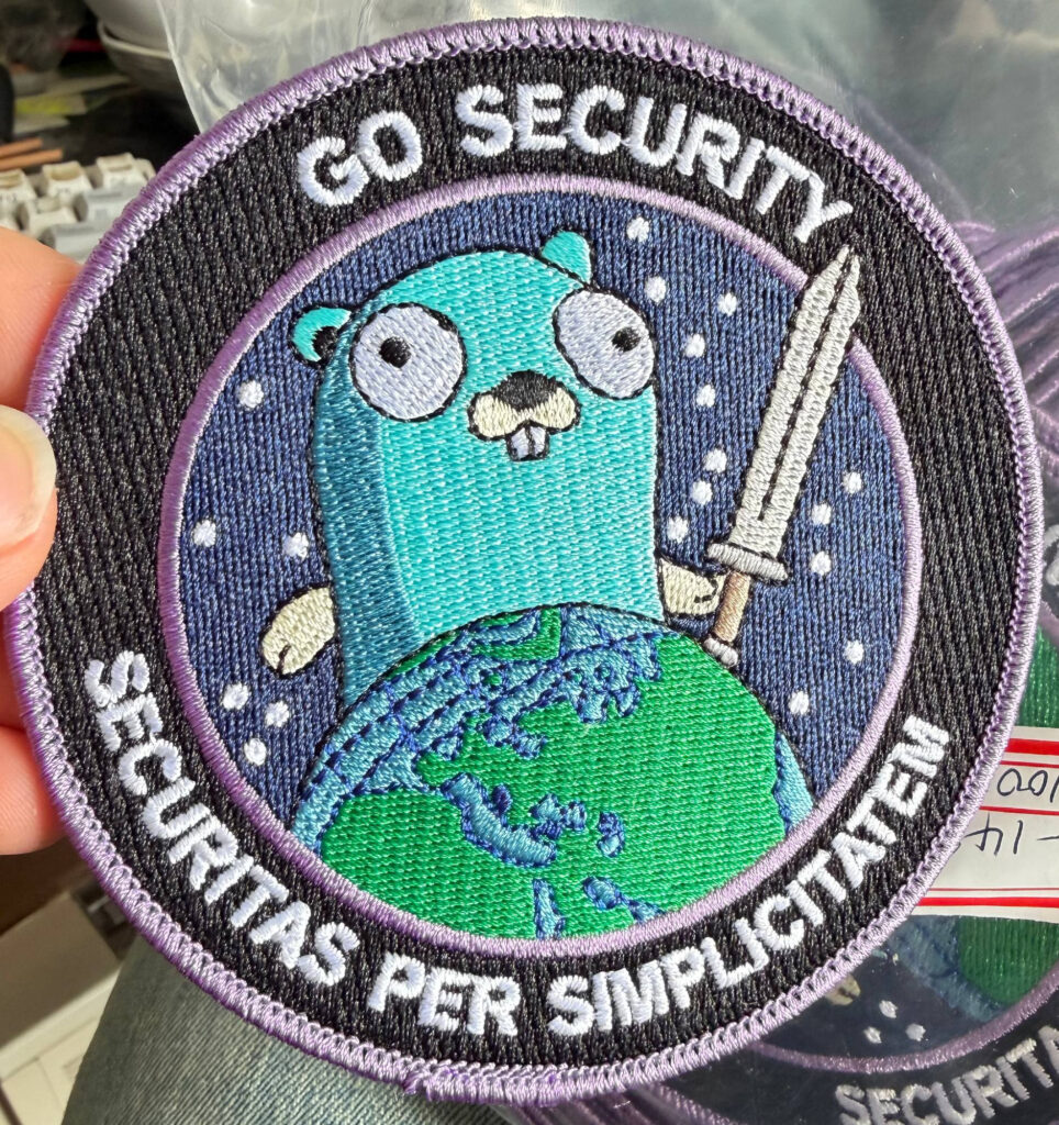A professionally embroidered patch depicting a cartoon gopher holding a sword and towering over the planet earth. Around the border of the patch reads "Go Security" at the top and "Securitas Per Simplicitatem" at the bottom. This patch has cleaner stitching and brighter colors compared to the original prototype.